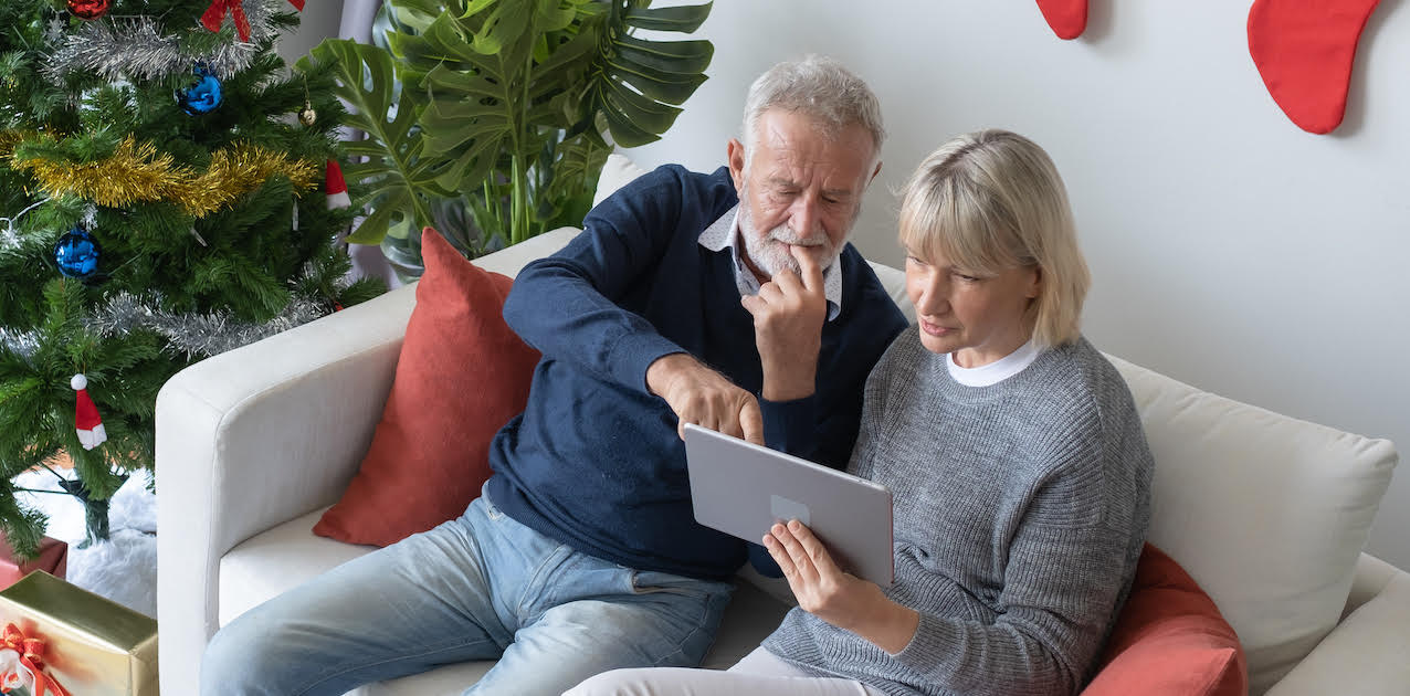 a man and a woman sitting on a couch together looking at a tablet device.