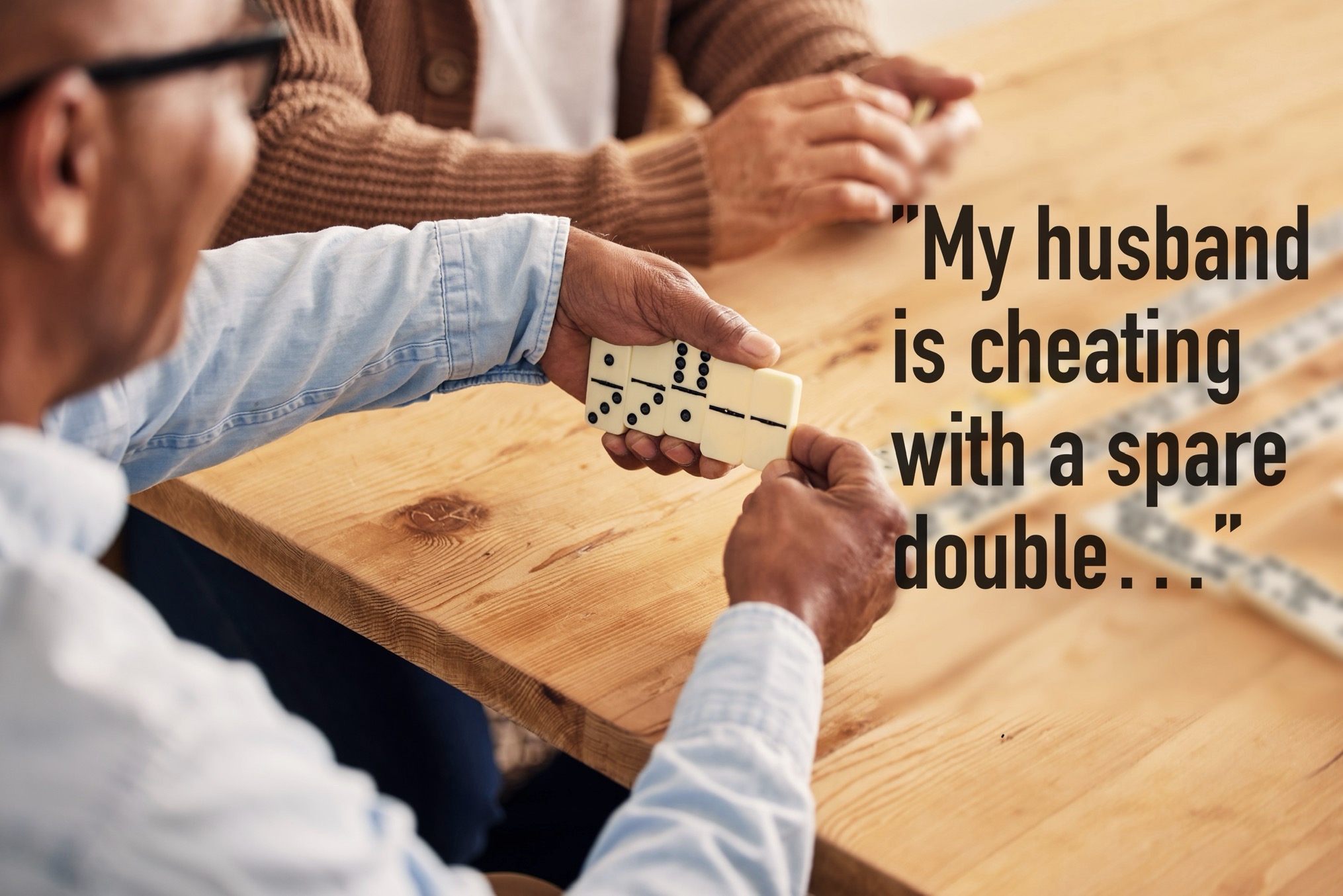Close-up of a man holding domino tiles during a Mexican Train Dominoes game with the humorous caption “My husband is cheating with a spare double…” printed beside him.