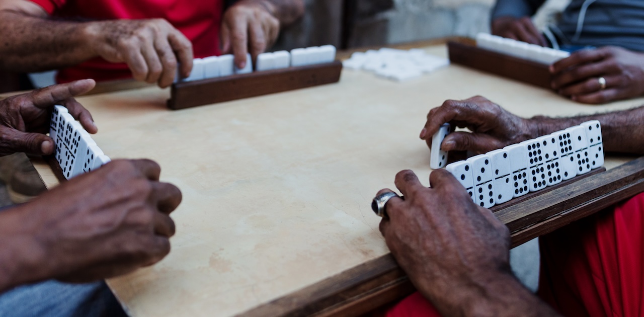 Four people playing dominoes at a table.