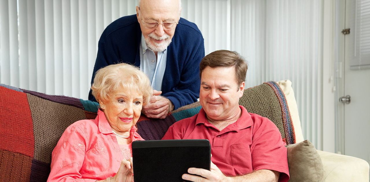 An adult son showing his senior parents games on a tablet.